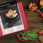 A red binder with a recipe and some vegetables on it