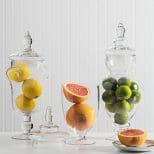 A table with three glass vases filled with fruit.