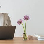 A person sitting at a desk with a laptop and flowers in a vase.