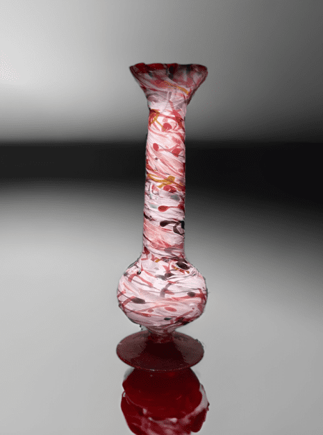 A glass vase with red and white speckles on it.