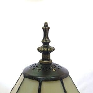 Close-up of an antique lamp finial made of dark metal with ornamental details, set against a soft white background.