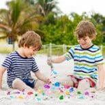 Two young boys playing with sand on the beach.