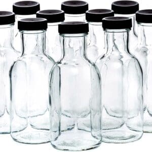 Sentence with product name: Several 16 oz clear glass bottles with black caps arranged in rows on a white background.