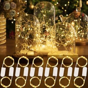 Warm led Micro LED Fairy Lights under glass domes on a wooden table, surrounded by wedding rings with attached blank tags.