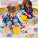 Two little girls playing in a sandbox with toys.