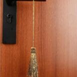 A golden Tassels hanging from the handle of a closed wooden door.