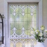 An ornate stained-glass window featuring geometric and floral designs, set within a white frame in a softly lit room created using the Gallery Glass Paint Most Popular Kit.