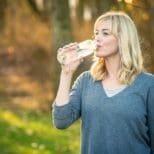 A woman drinking water from a glass in the woods.