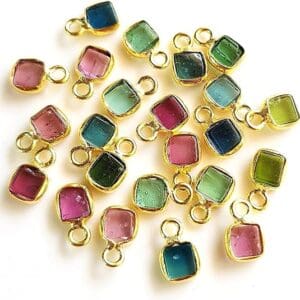A collection of colored gems charms with gold borders, scattered on a white background.