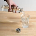 A person pouring water into a glass on top of a table.