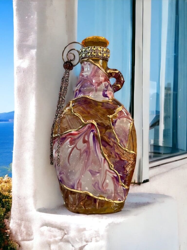 Decorative multicolored glass bottle with a golden cap, placed on a windowsill with a scenic blue sky background.