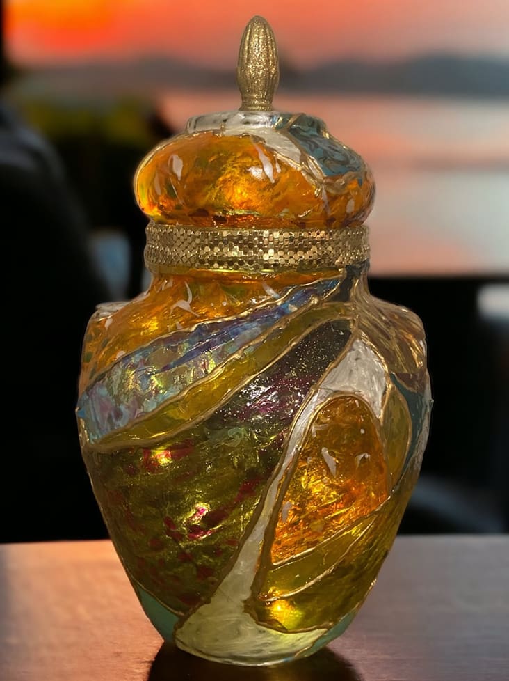 Decorative glass jar with a golden lid, featuring swirling colors, set against a blurred sunset background.