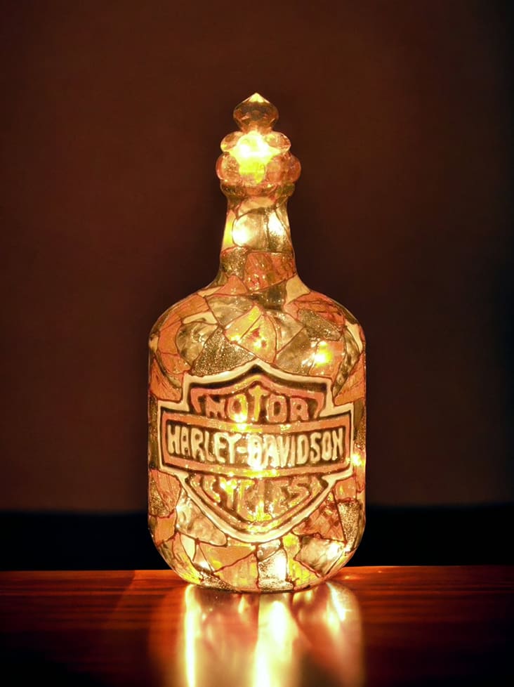 Illuminated glass bottle with a harley davidson logo, featuring a mosaic design, placed against a dark background.
