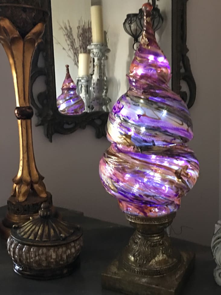 A decorative glass sculpture with swirling purple and pink patterns, displayed on a table next to a candlestick and vases.