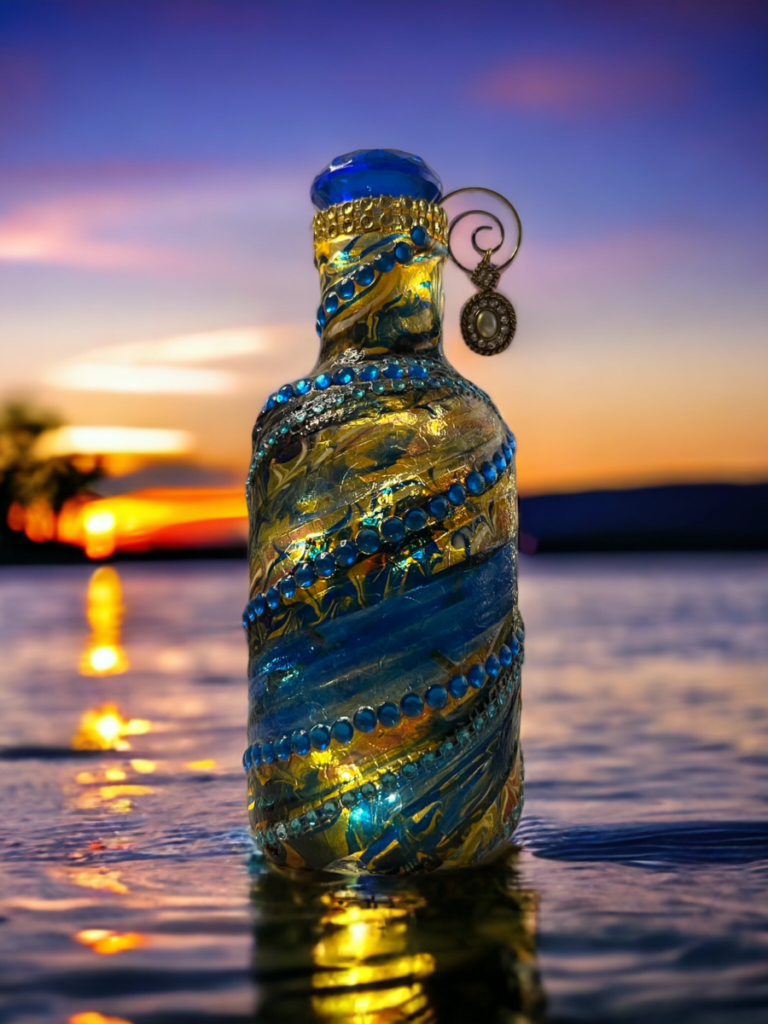 Decorative glass bottle with intricate blue patterns and a hanging earring, standing on a wet surface with a sunset reflecting in the background.
