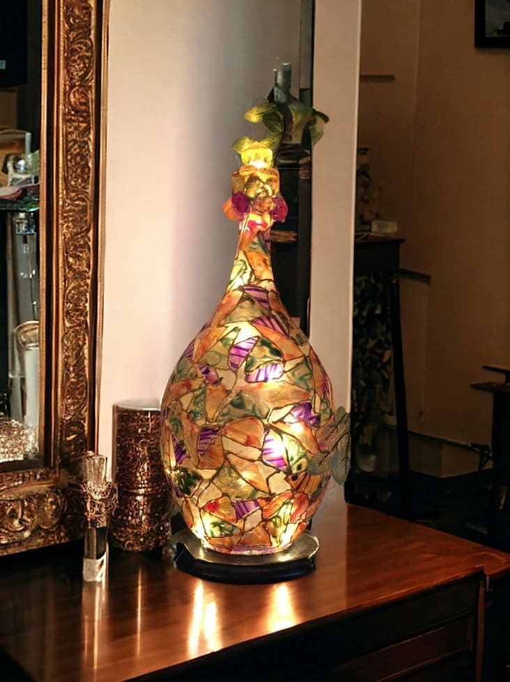 An ornate, illuminated glass lamp with floral motifs on a wooden table, flanked by a mirror and small candles.